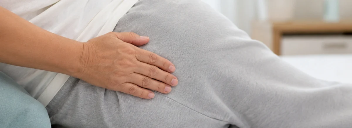 Person lying on their side in bed with a hand resting on the hip area, illustrating body positioning and pressure points associated with Pressure Ulcer Stages and pressure injury prevention.